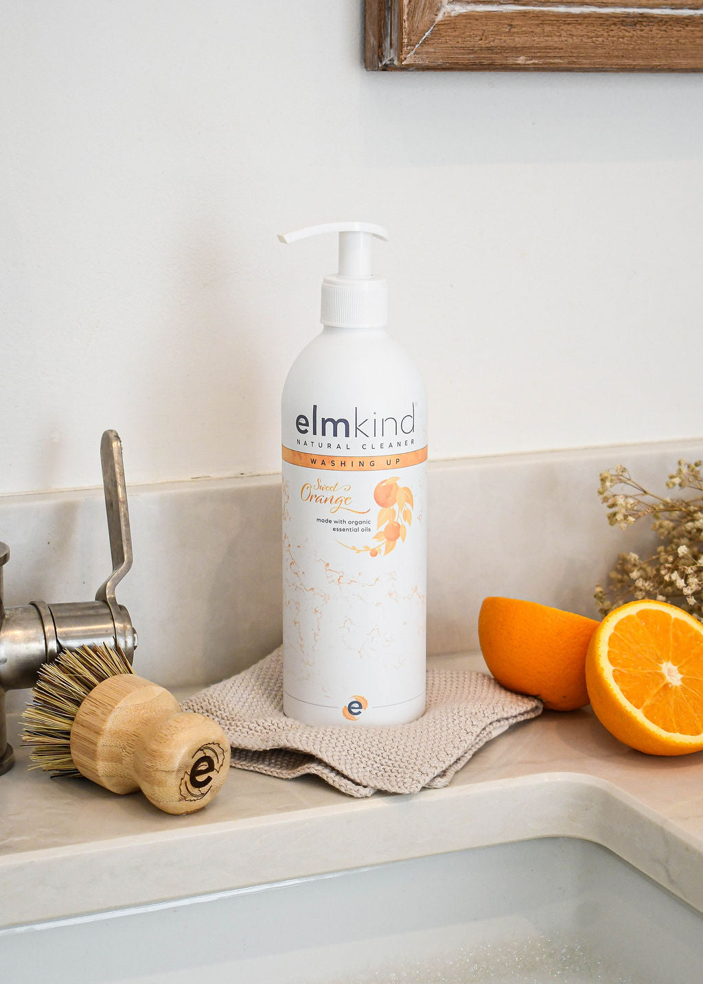 an elmkind scrubbing brush on a kitchen side with some dried flowers, freshly cut oranges and an elmkind sweet orange washing up liquid