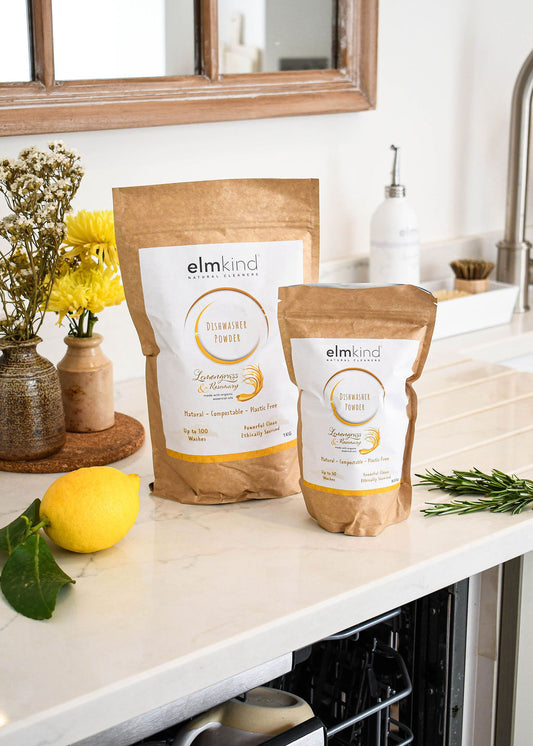 two bags of elmkind dishwasher powder 1KG and 500g, with lemongrass and, rosemary essential oils in a brown plastic free paper bag by a dishwasher