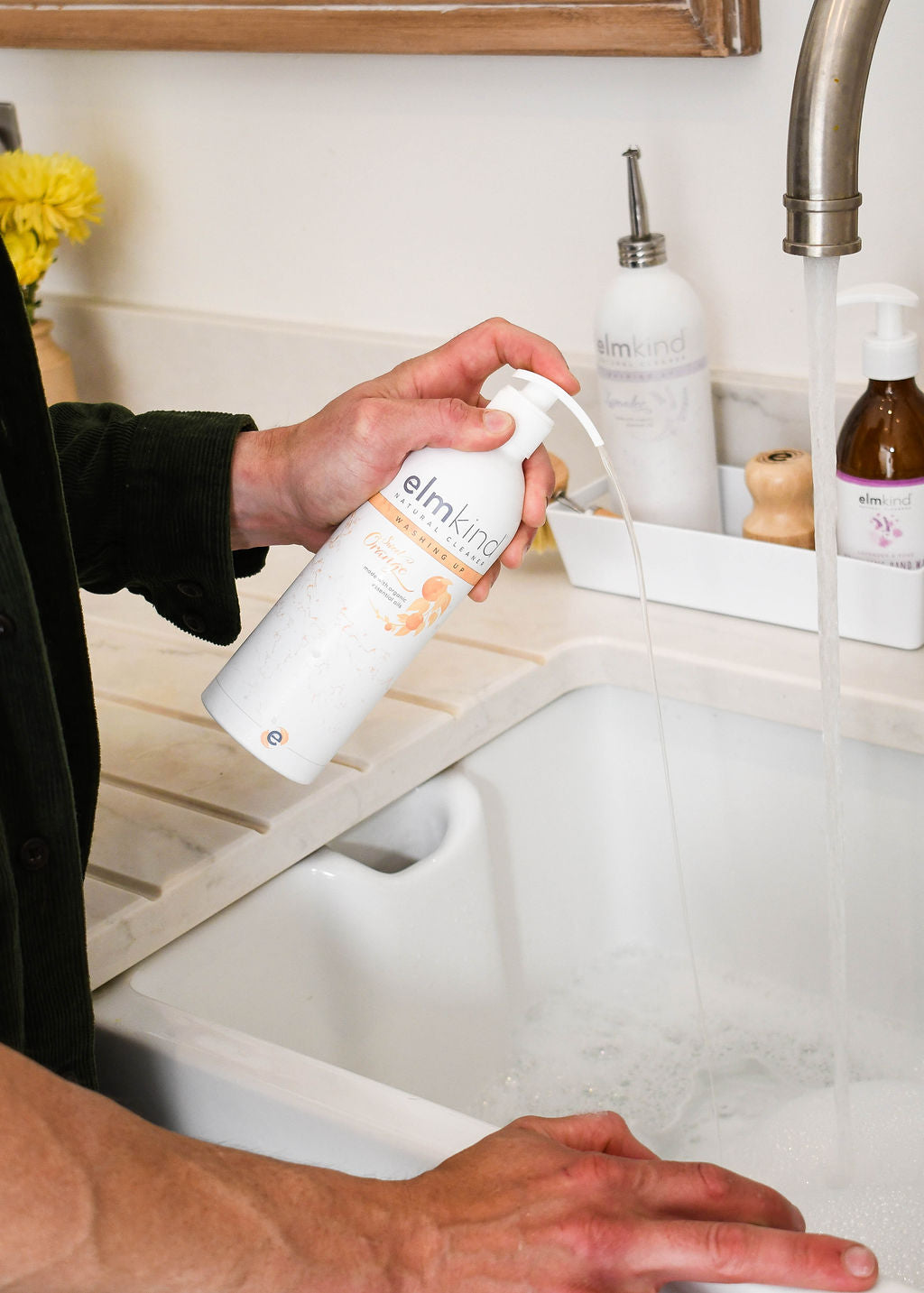 A man squirting some elmkind sweet orange washing up liquid into a foamy sink of bubbles