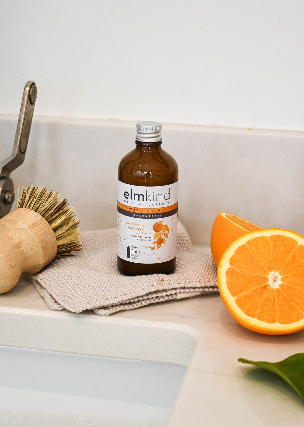 A concentrated amber glass refill bottle of natural sweet orange washing up liquid alongside some freshly cut oranges