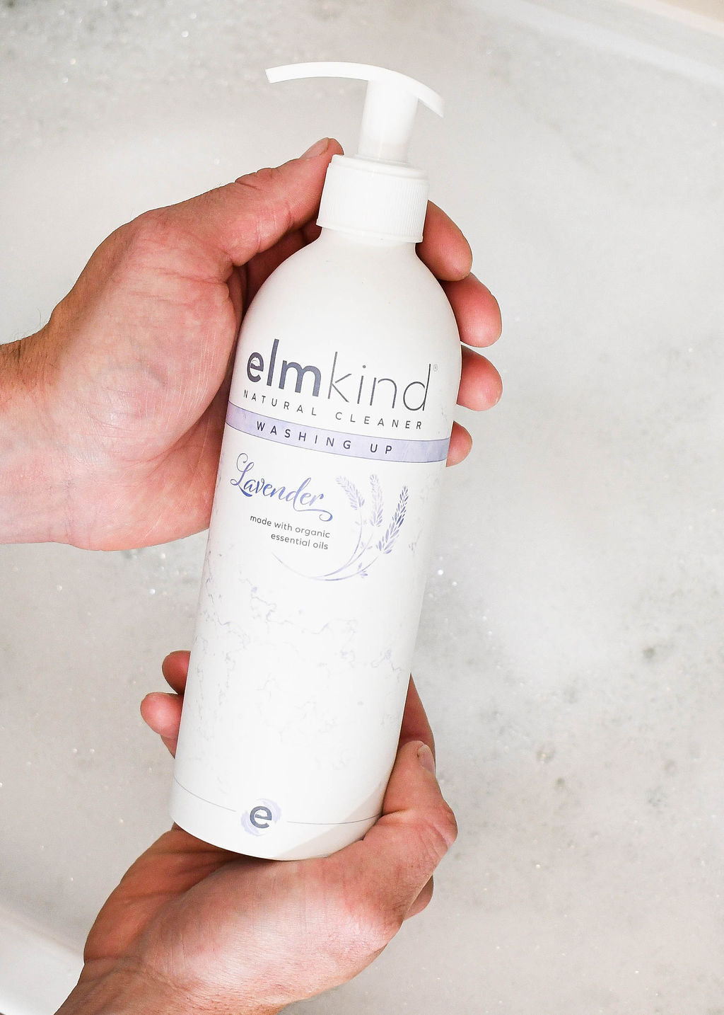 elmkind Lavender washing up liquid in aluminium bottle with plastic pump in a mans hands over a sink full of bubbles 