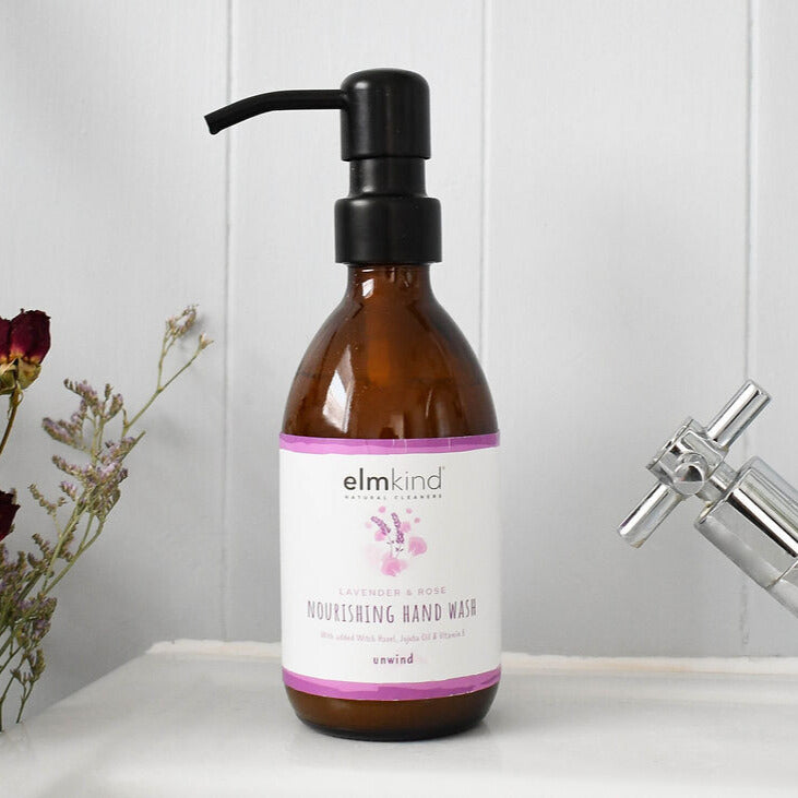 elmkind Lavender and Rose hand wash in a 250ml amber glass bottle with black metal pump on a bathroom sink with a rose in the background