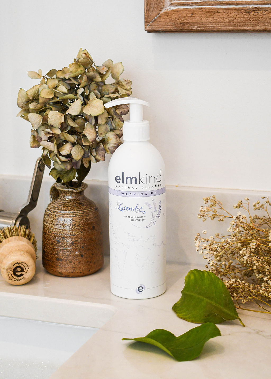 elmkind Lavender washing up liquid with plastic pump on kitchen side with dried flowers and an elmkind scrubbing brush