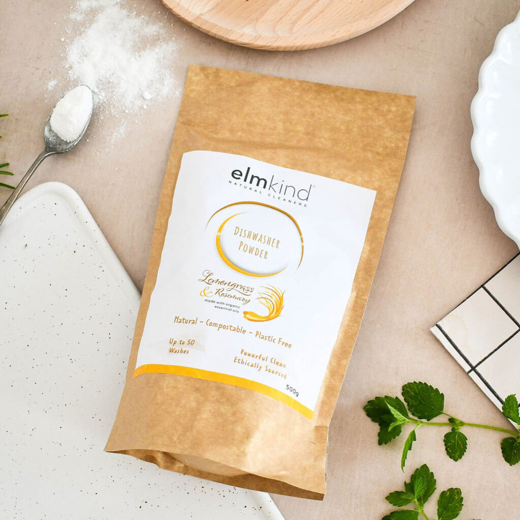 elmkind dishwasher powder 500g, with lemongrass and rosemary essential oils in a brown plastic free paper bag on a kitchen surface with some white powder showing on a spoon