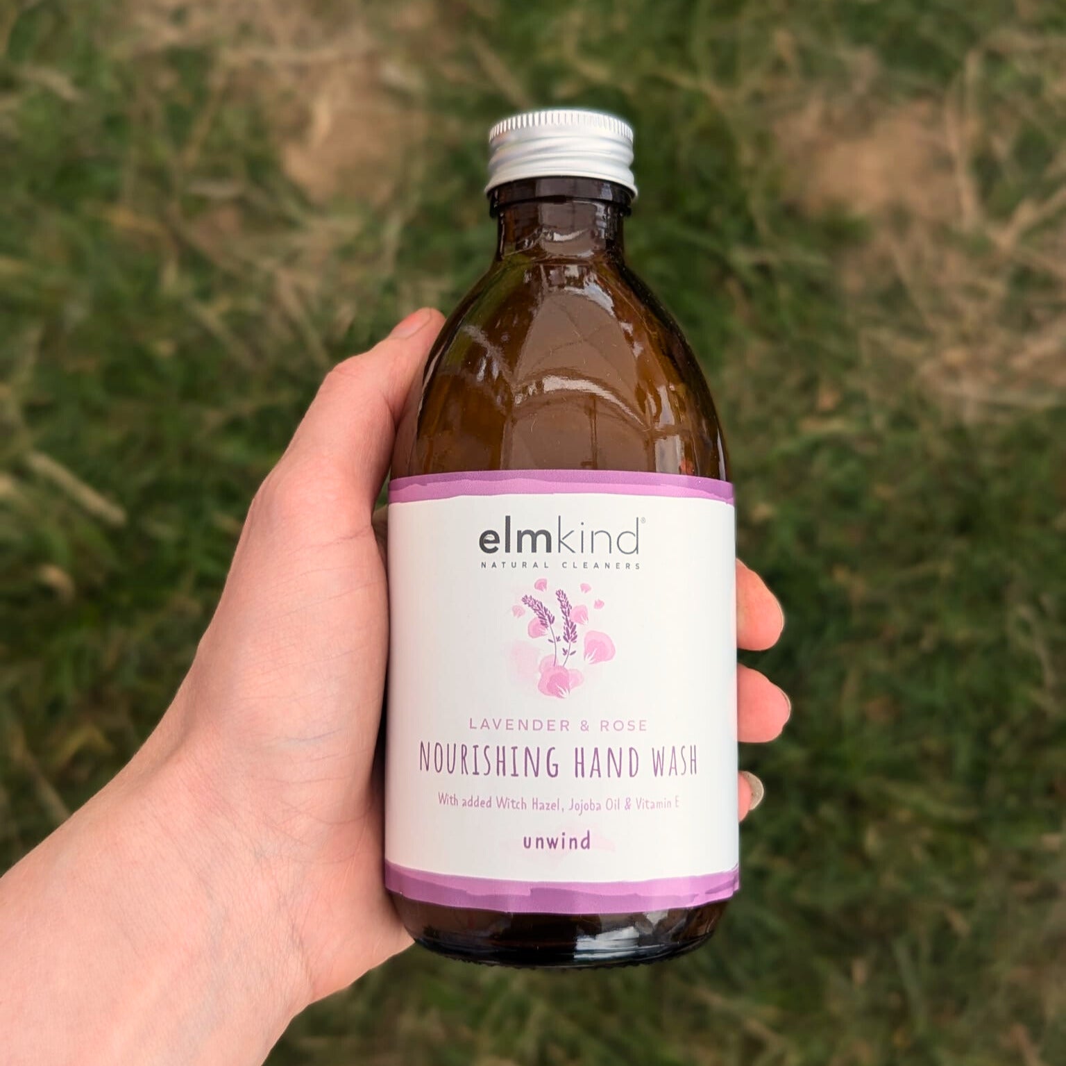 elmkind Lavender and Rose hand wash in a 250ml amber glass bottle with a metal cap in a woman's hands with grass in the background