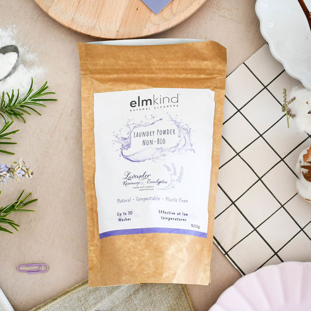 elmkind laundry powder 500g, with lavender, rosemary and eucalyptus essential oils in a brown plastic free paper bag on a kitchen side with rosemary sprigs and lavender flowers