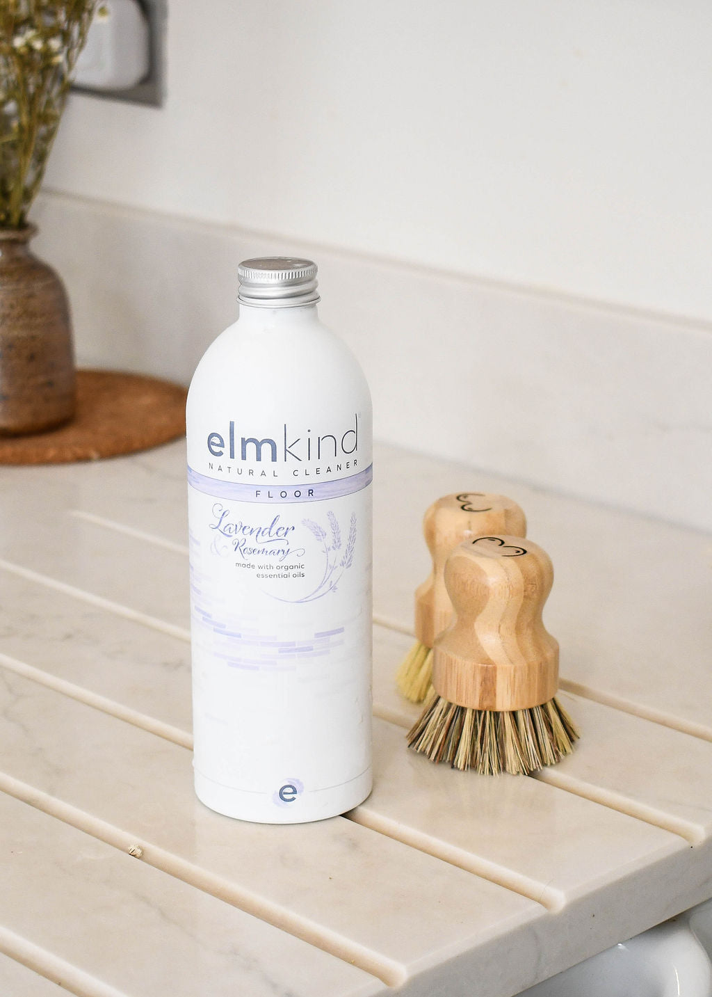 a pair of elmkind scrubbing brushes with breasts designed onto the handle to support breast cancer awareness, sat on a kitchen side with an elmkind floor cleaner bottle