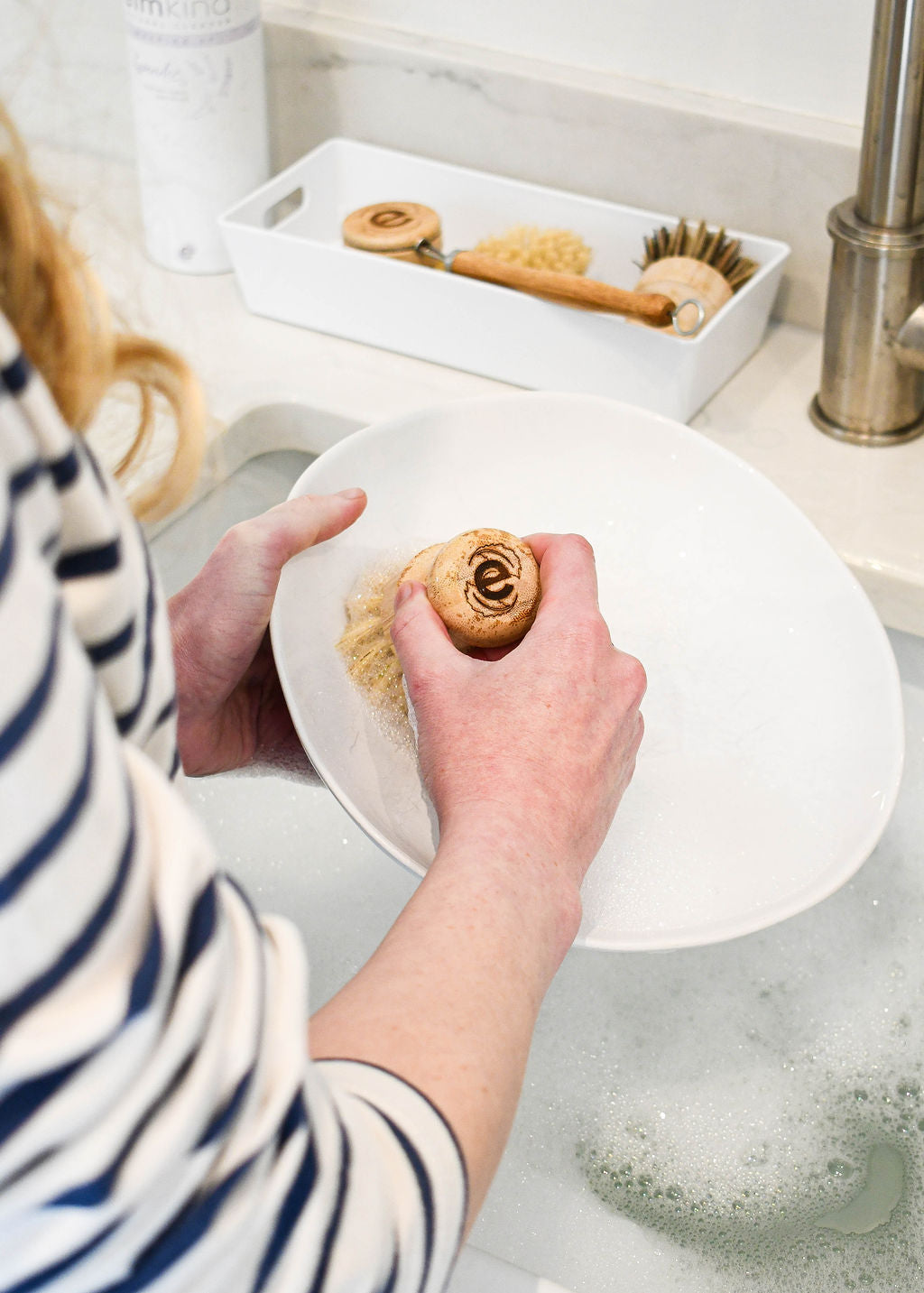a woman washing up with an elmkind scrubbing brush, scrubbing a plate