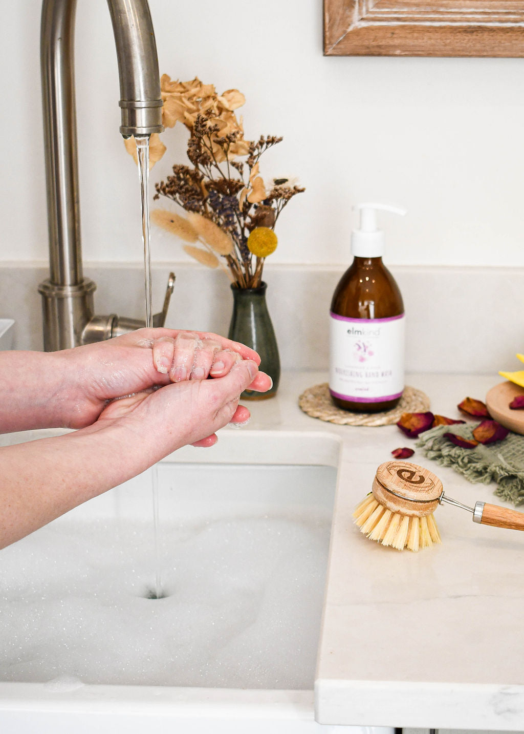 a woman washing her hands with plant based non toxic handwash, with elmkind hand was bottle in the background